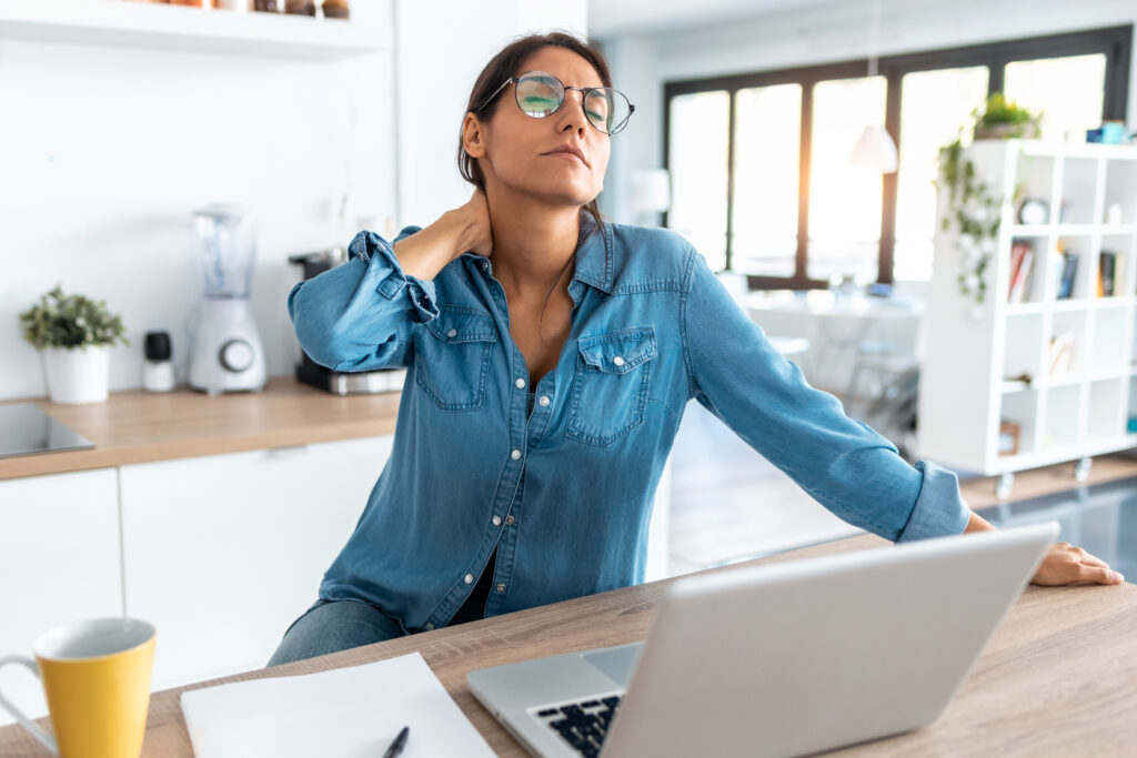 Shot of tired business woman with neck pain looking uncomfortable while working from home on laptop.