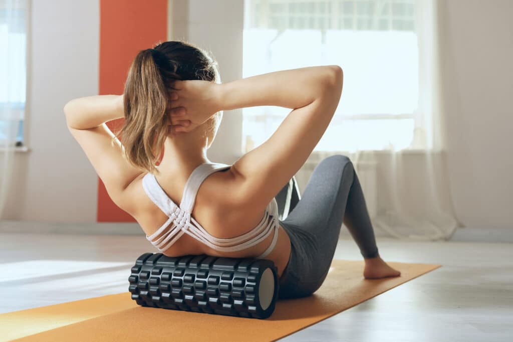 Woman performs myofascial release of hyper-flexible muscles of the back with a massage roller in the studio. The concept of back fatigue prevention and self-massage.