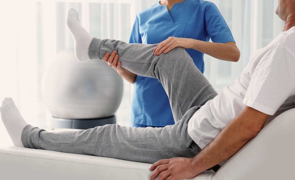 A patient having his right leg stretched and examined by a nurse in blue scrubs