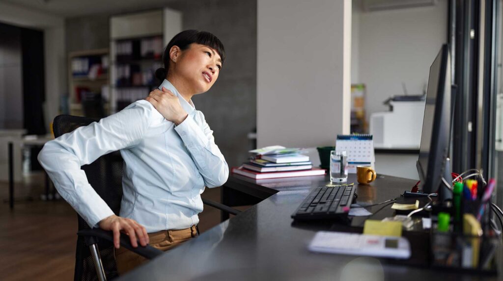 an Asian female home office working stretching her neck at her computer desk