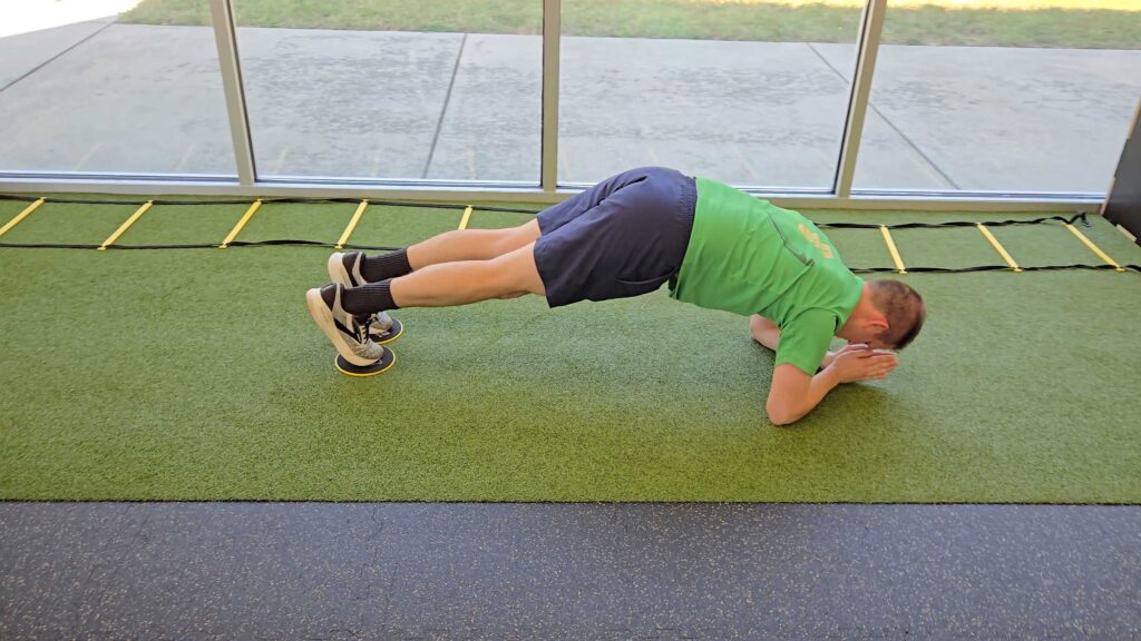 Male Patient performing a Body Saw Slider Plank in a medical facility gym