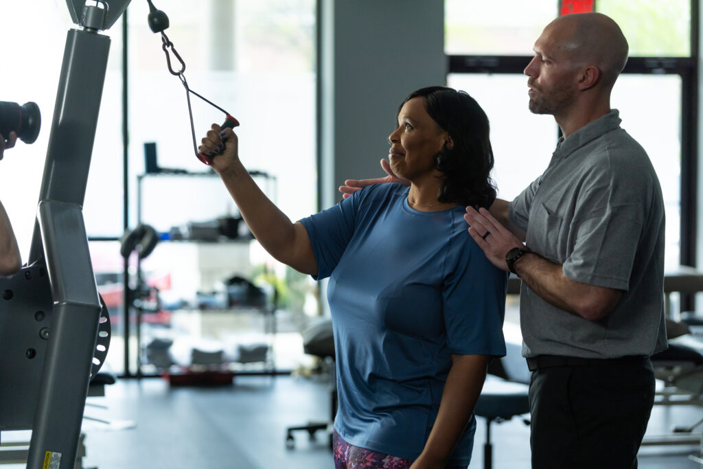 Woman using cable machine while male physical therapist supervises