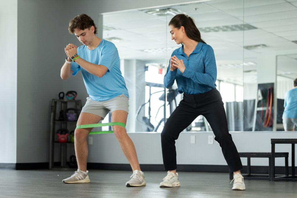 Male using exercise band on legs while female physical therapist coaches