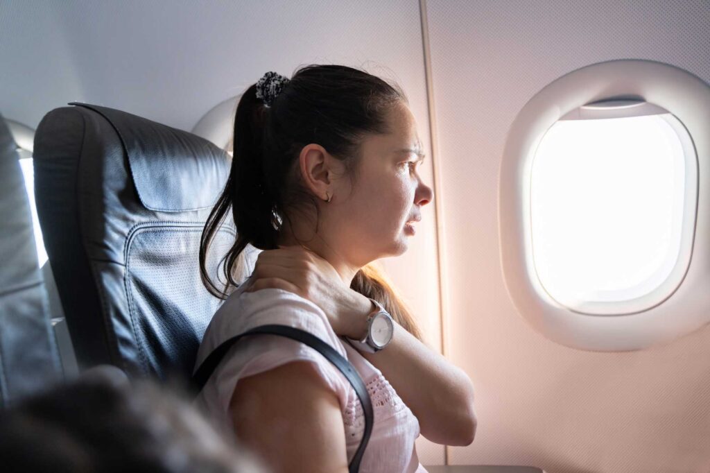 A female traveler on a plane holding her neck in pain