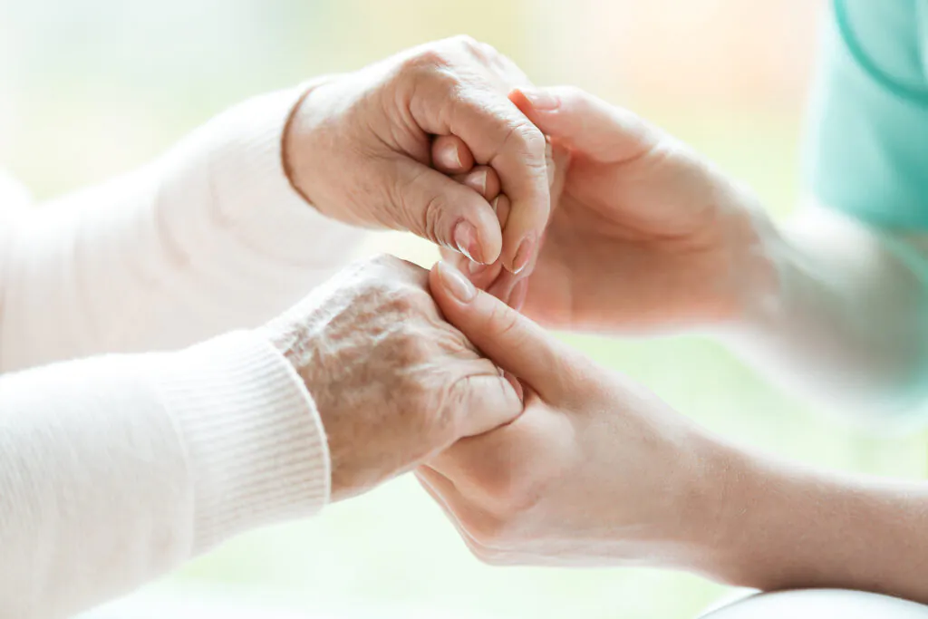 Close-up of a younger person's hands gently holding an older person's wrinkled hands, symbolizing care and support.