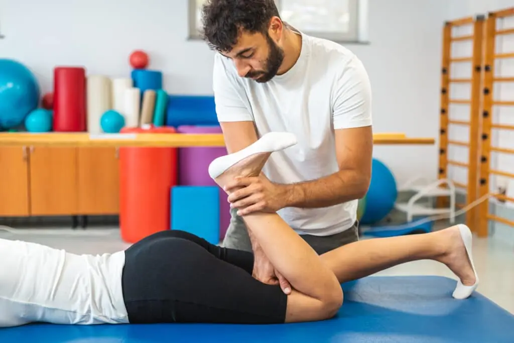 Male physiotherapist giving exercise therapy for sciatica to a female patient in a supine position.