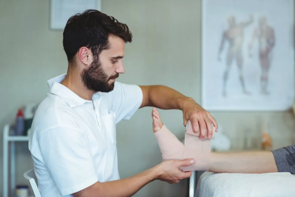 Physiotherapist putting bandage on injured feet of patient