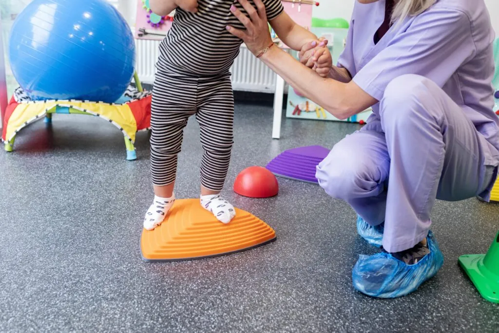 Child balancing on sensory board with caregiver.