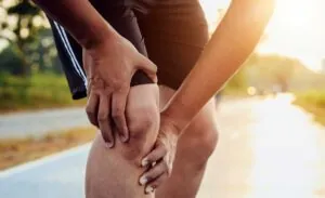 A man reaching for his injured knee while on a run during a sunny day