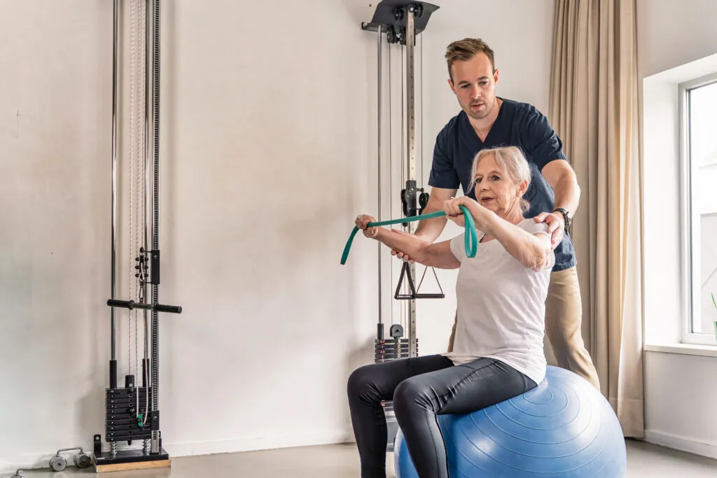 Senior woman doing resistance band exercise with physiotherapist support during rehabilitation occupational therapy session.
