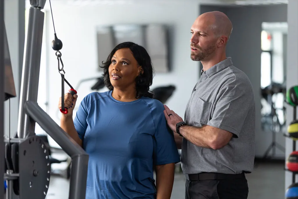 A female patient being aided with a pulldown weight exercise by a male physical therapist
