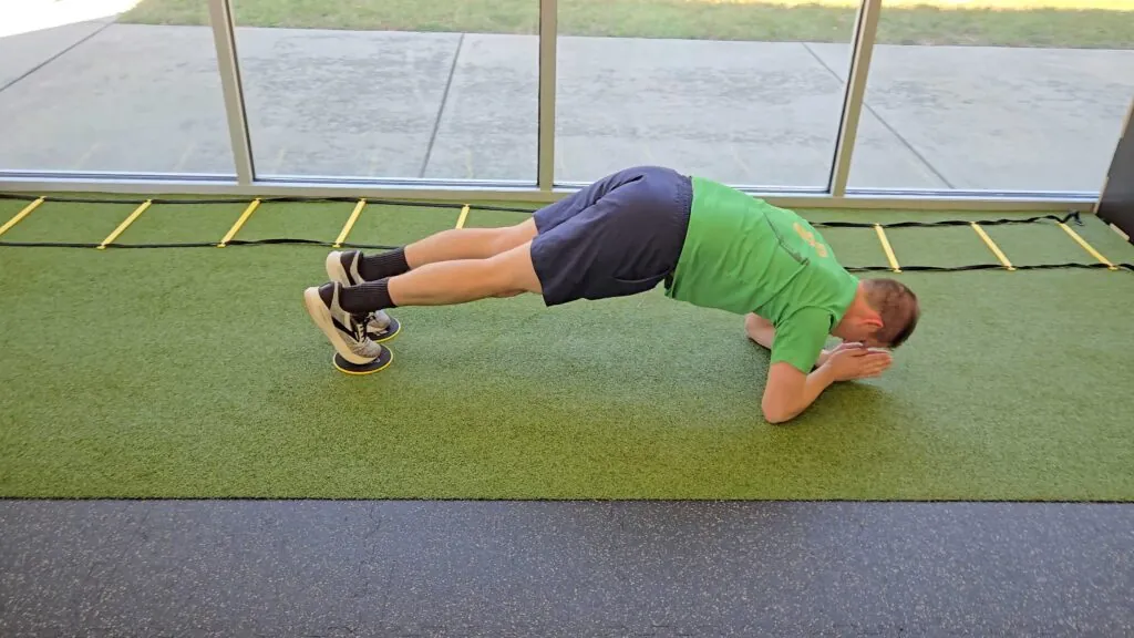 Male Patient performing a Body Saw Slider Plank in a medical facility gym