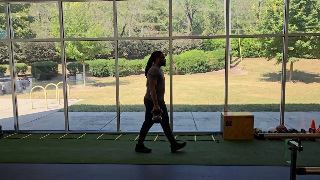 Male Patient performing a Suitcase Carry with Kettle bells in a medical facility gym