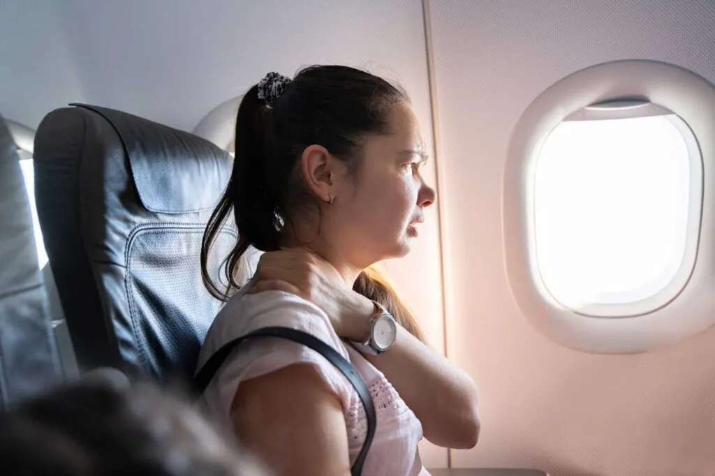 A female traveler on a plane holding her neck in pain