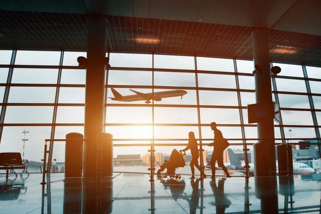 photo of a plane landing at an airport through a window view with travelers in the foreground