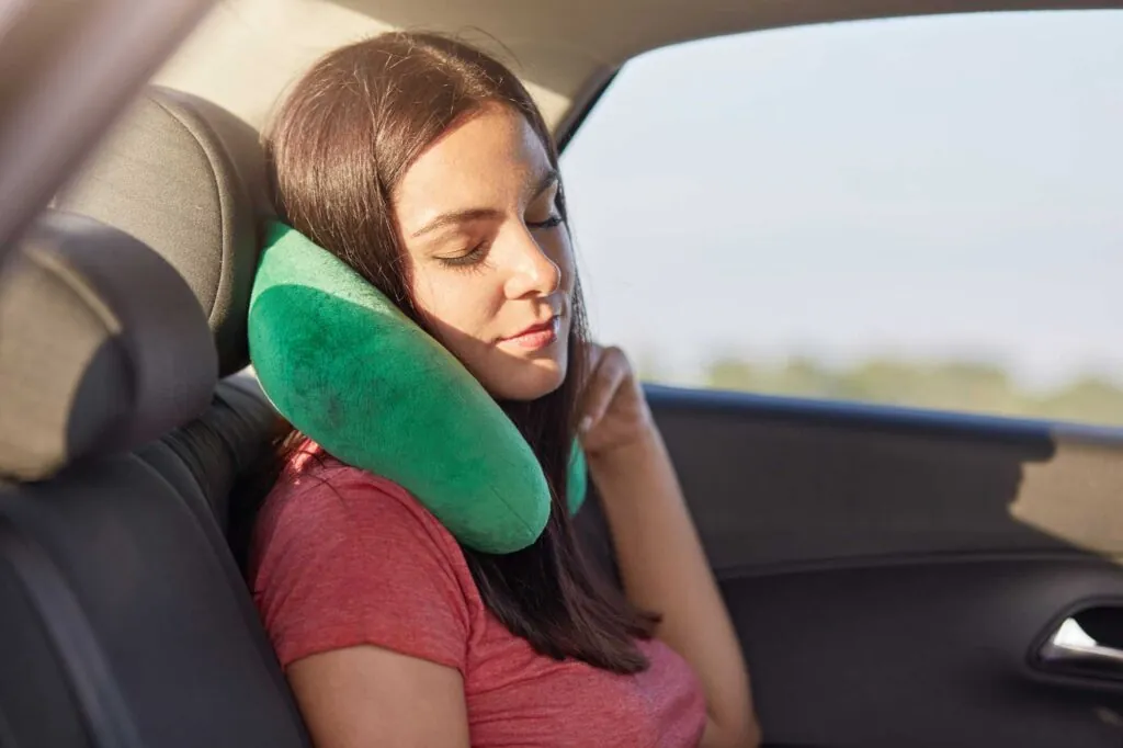 Female passenger in a car, wearing a neck pillow