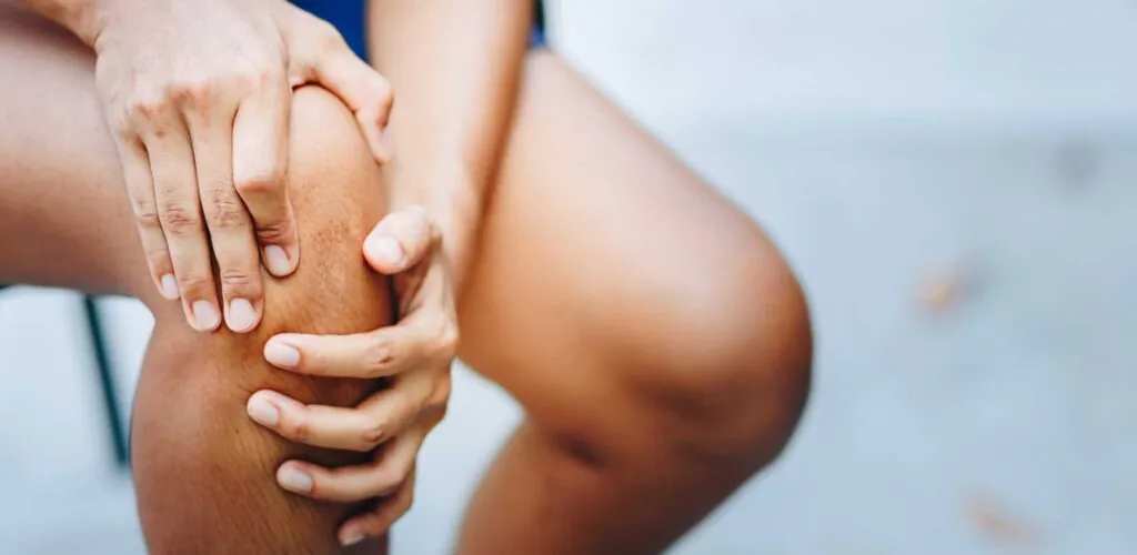 A person compressing their knee with their hands due to knee pain.