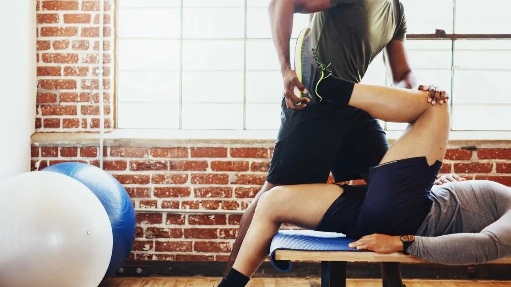African American trainer assists with leg stretches. Diverse people training in a gym. Fit athlete doing fitness workout. Fit athlete doing fitness workout, training in a gym.