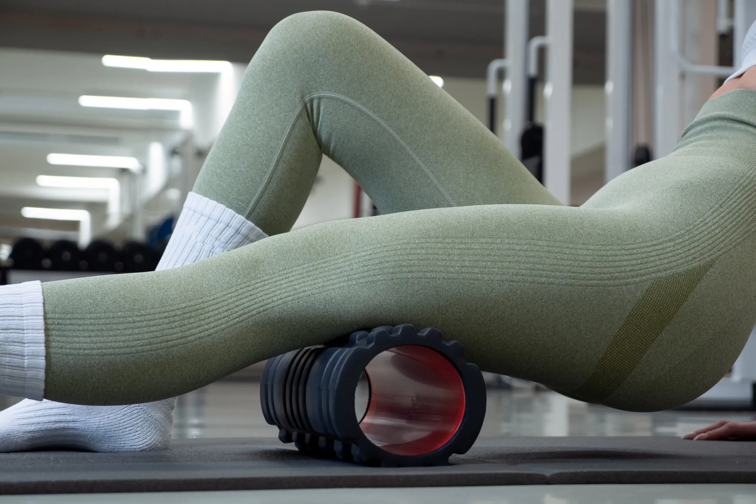 Cropped shot of a woman uses foam roller for exercising stretches. Massages muscles on hips and legs in gym tries to remove pain. Healthy lifestyle rehabilitation.