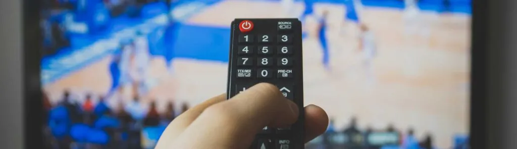 Male hand holding TV remote control. Basketball match.