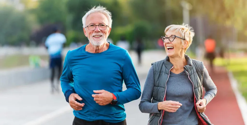 Cheerful active senior couple jogging together outdoors along the river. Healthy activities for elderly people.