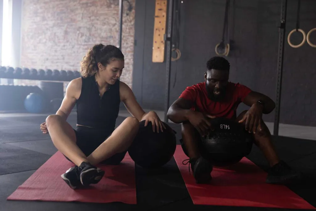 a man and woman sitting on a gym floor working out with medicine balls