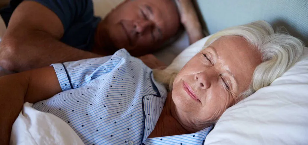 Senior white couple lying asleep in their bed, waist up, close up