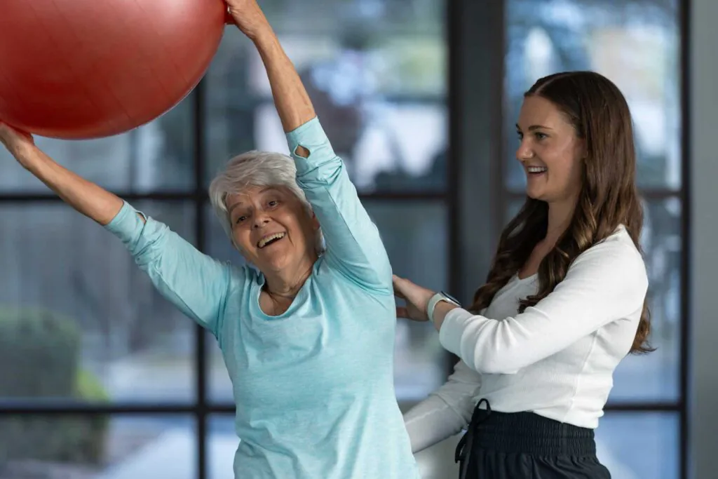 a senior patient doing balance exercises with a Pilates ball under PT supervision