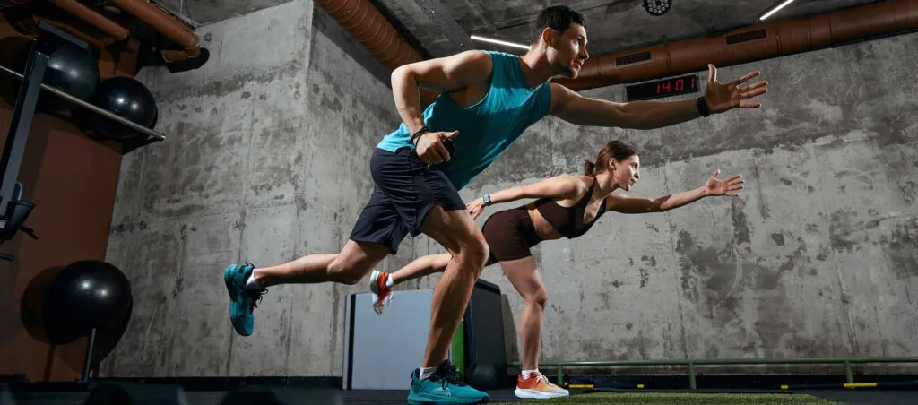 Man and woman performing functional training movement with forward reach in gym. Concept of mobility training, balance development, fitness program and athletic performance.
