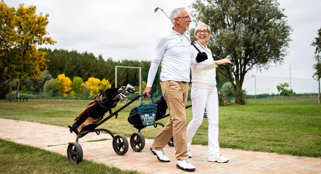 An elegant senior couple enjoying free time in retirement by playing golf and walking to the practice range.