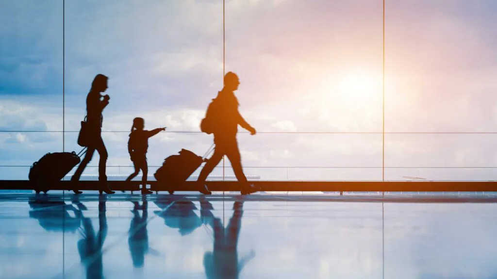 A family traveling through an airport, silhouetted by a bright sun shine through the window