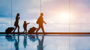 A family traveling through an airport, silhouetted by a bright sun shine through the window