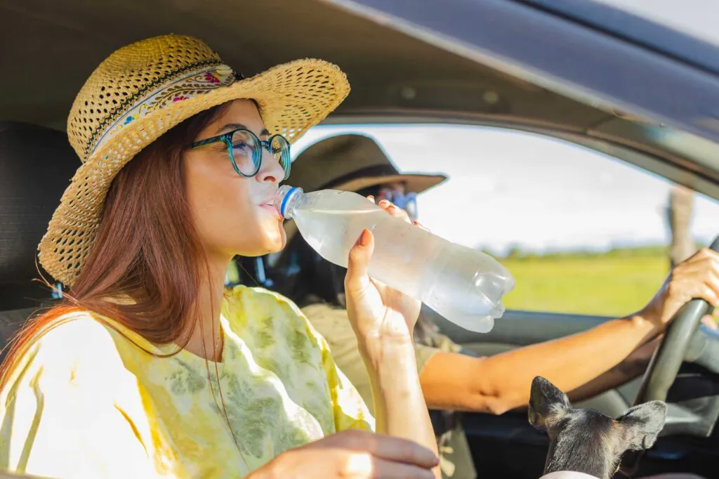 passenger in a sun hat hydrating with a water bottle while traveling by car
