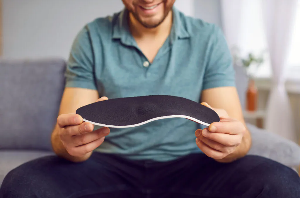 A smiling man holds a black and white orthopedic insole, showing its contoured shape.