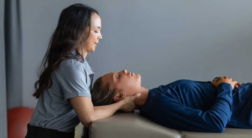 A woman lying on her back receives neck support from a practitioner.