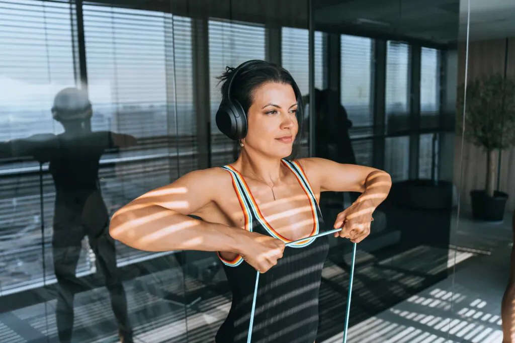 Purposeful young brunette hispanic woman training at hotel room with rubber tape expander tools away with confident face expression. Sports, fitness, active people.