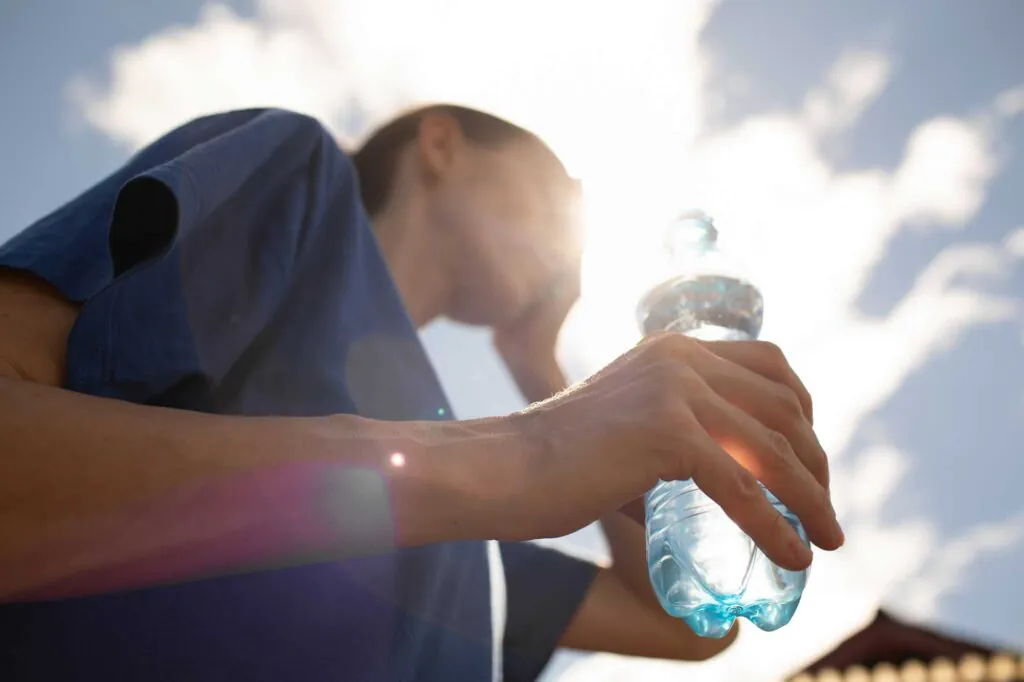 Young woman feeling exhausted tired from the heat holding bottle of water 