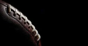 Close-up of a brown American football with white laces against a black background.