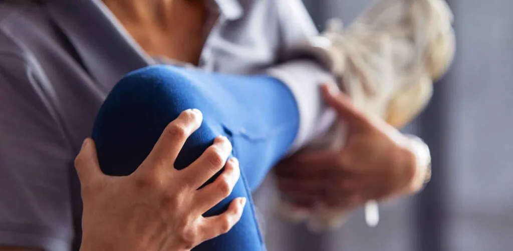 A person's leg in blue pants is held by two hands, suggesting physical therapy or stretching.