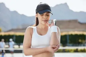 A woman in tennis attire holds her elbow with a tennis racket in hand on a court suffering from Tennis Elbow.