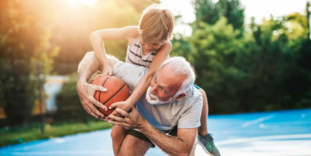 An older man and a young boy playing basketball together on an outdoor court.