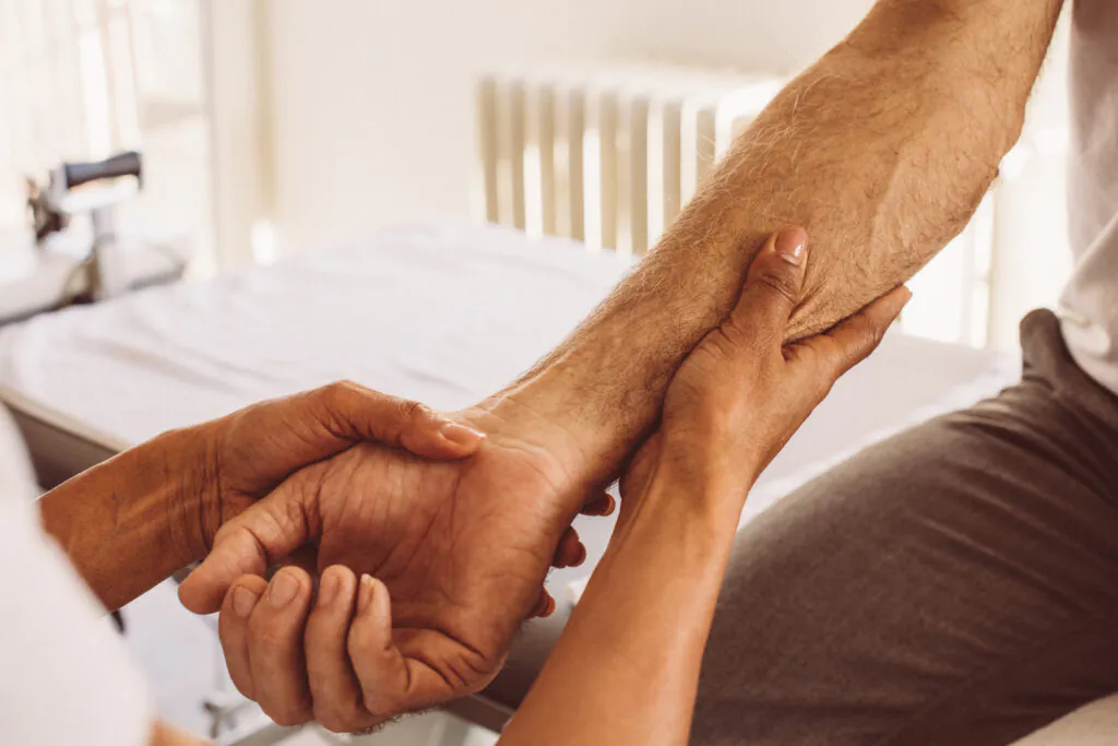 Close-up of a person's hands examining another person's wrist and forearm in a medical setting.