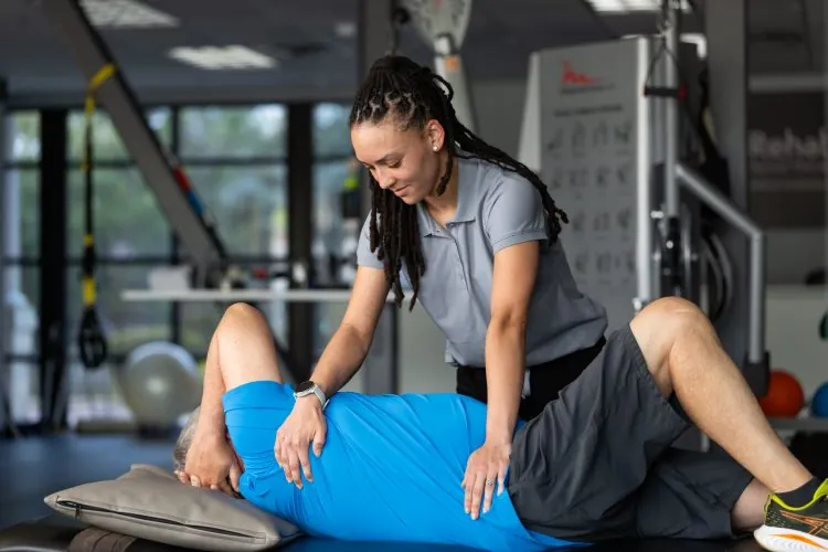 Female African American PT helping an older patient with a back and shoulder stretch on a medical table
