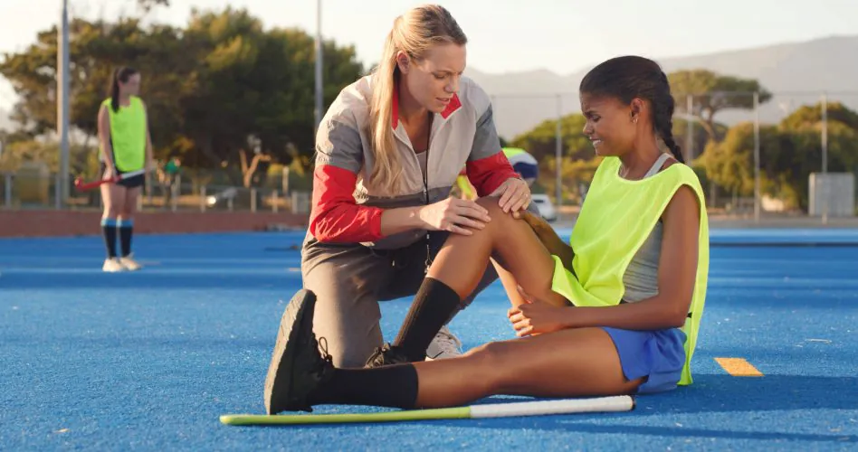 Women, sports coach, and player with knee pain, accident and help with training. People, hockey athlete or medical assistance with support, joint injury or torn muscle with tension, outdoor or strain.